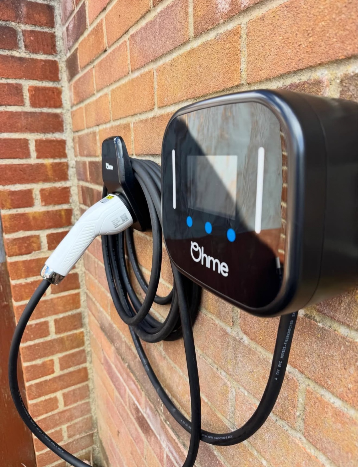 Tethered Ohme EV charger installed on a brick wall